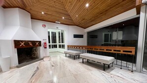 A modern interior with a fireplace, marble flooring, wooden ceiling, and a bench by a window. - Hotel Buzio (Sines)