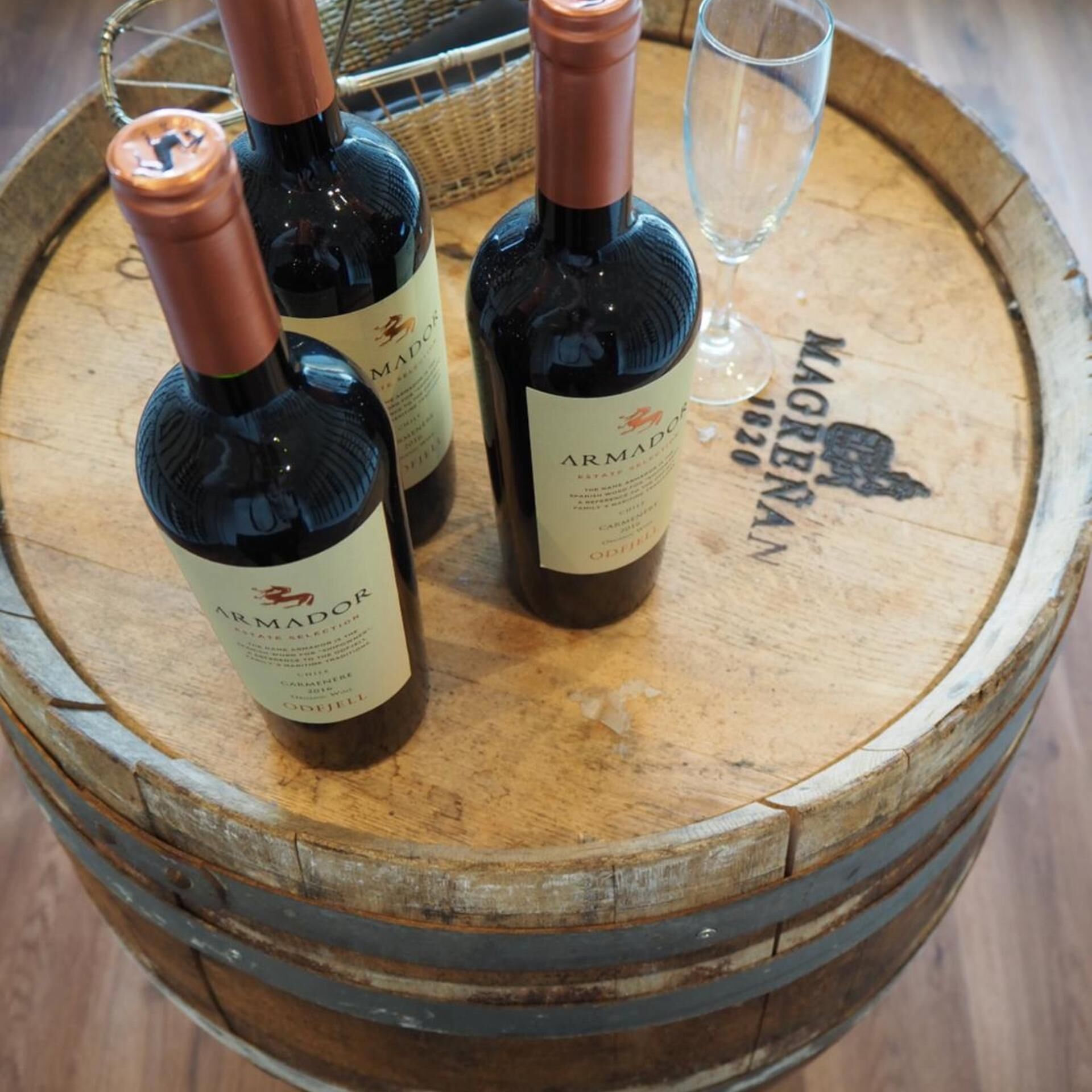 Tres botellas de vino Armador sobre un barril de madera, con una copa y un sacacorchos.