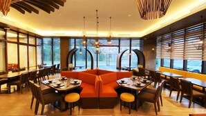 A modern dining area with a central orange seating area, wooden tables, and chairs. - The Aurora Subic Hotel Managed by HII (Olongapo)