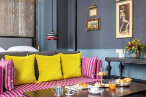 A room with a striped sofa, a table with breakfast items, and a wall with framed pictures. - Palazzo Roma (Rome)