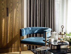 A modern room with a blue upholstered chair, a wooden wardrobe, a glass coffee table with a magazine, and a decorative tray with items. - Nex Hotel Istanbul City Center (Istanbul)