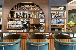 A bar area with a coffee machine, shelves of liquor bottles, and three blue chairs. - Nex Hotel Istanbul City Center (Istanbul)
