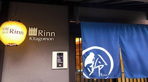 Un mur sur lequel est inscrit le nom « Rinn Kitagomon » et une bannière bleue ornée d’un logo.