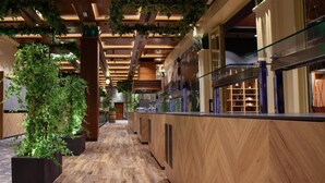 A modern hotel lobby with a wooden floor, black planters with greenery, and a glass display case with wine glasses. - Park Casino And Hotel (Nova Gorica)