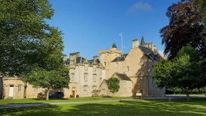 A large, historic building with multiple towers and a flagpole, surrounded by well-maintained lawns and trees. - Golf View Hotel & Macintosh Restaurant (Lossiemouth)