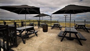 An outdoor patio with picnic tables and umbrellas, overlooking a coastal landscape. - Golf View Hotel & Macintosh Restaurant (Lossiemouth)