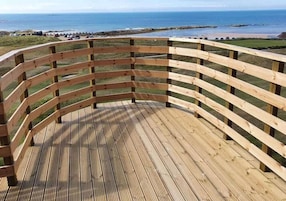 A wooden deck with a curved railing overlooking a beach.