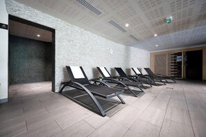 A modern waiting area with a row of lounge chairs against a textured wall, a clock, and a wooden door. - Nemea Biarritz Les Hauts de Milady (Biarritz)