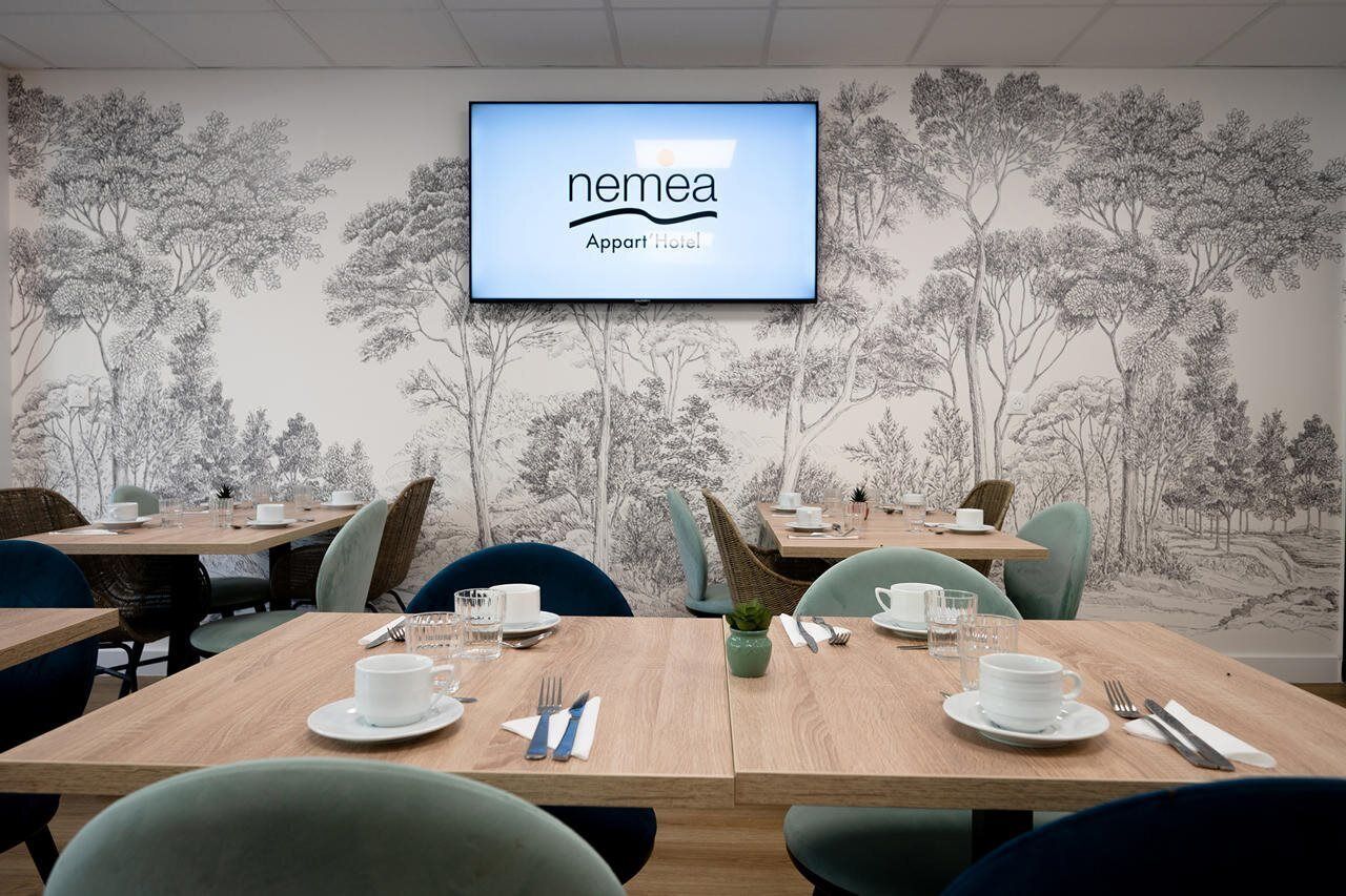 Una sala conferenze con un grande schermo che mostra il logo NMEA, circondata da tavoli allestiti per riunioni, con un murale raffigurante alberi sulla parete.