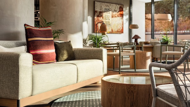A modern living room with a sofa, coffee table, and chairs. There is a large window with a view of trees and a painting on the wall. - Holiday Inn Beja (Beja)