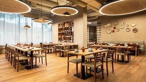 A restaurant with wooden tables and chairs, pendant lights, a bookshelf, and wall-mounted plates. - Holiday Inn Beja (Beja)