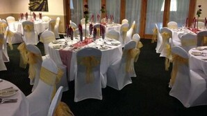 A banquet hall with round tables set for a formal event, each with white tablecloths and gold sashes on the chairs. - Bells Hotel (Coleford)