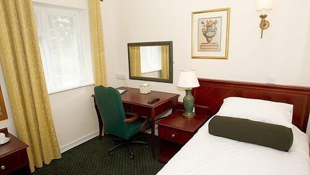 A hotel room with a bed, a desk, a chair, a lamp, a mirror, and a picture on the wall. - Bells Hotel (Coleford)