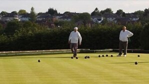 A group of people playing bowls on a green lawn with houses in the background. - Bells Hotel (Coleford)