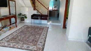 A spacious living area with a large rug, a staircase, a TV, and a kitchen in the background. - Homestay Selesa KBB 2 Guest House (Kuala Terengganu)