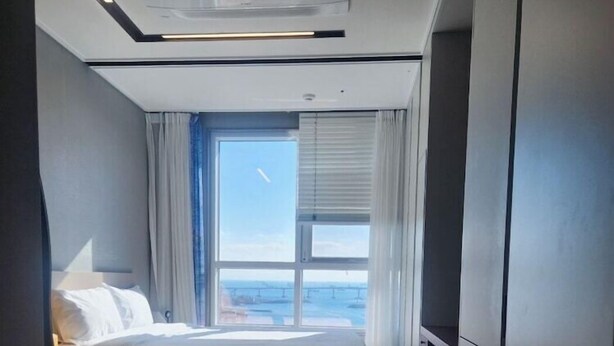 A modern hotel room with a bed, a glass coffee table, and a view of the sea through large windows. - The Bayment Residence (Busan)