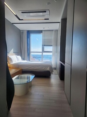 Een moderne hotelkamer met een bed, een glazen bijzettafeltje en uitzicht op de zee door grote ramen.
