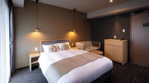 Hotellihuone, jossa on suuri sänky, yöpöydät, sohva, työpöytä ja vaatekaappi.