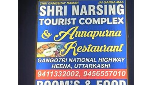 Une enseigne indiquant le complexe touristique Shri Narsing et le restaurant Annapurna, avec les numéros de téléphone et les services proposés, tels que la disponibilité des chambres et les options de restauration.