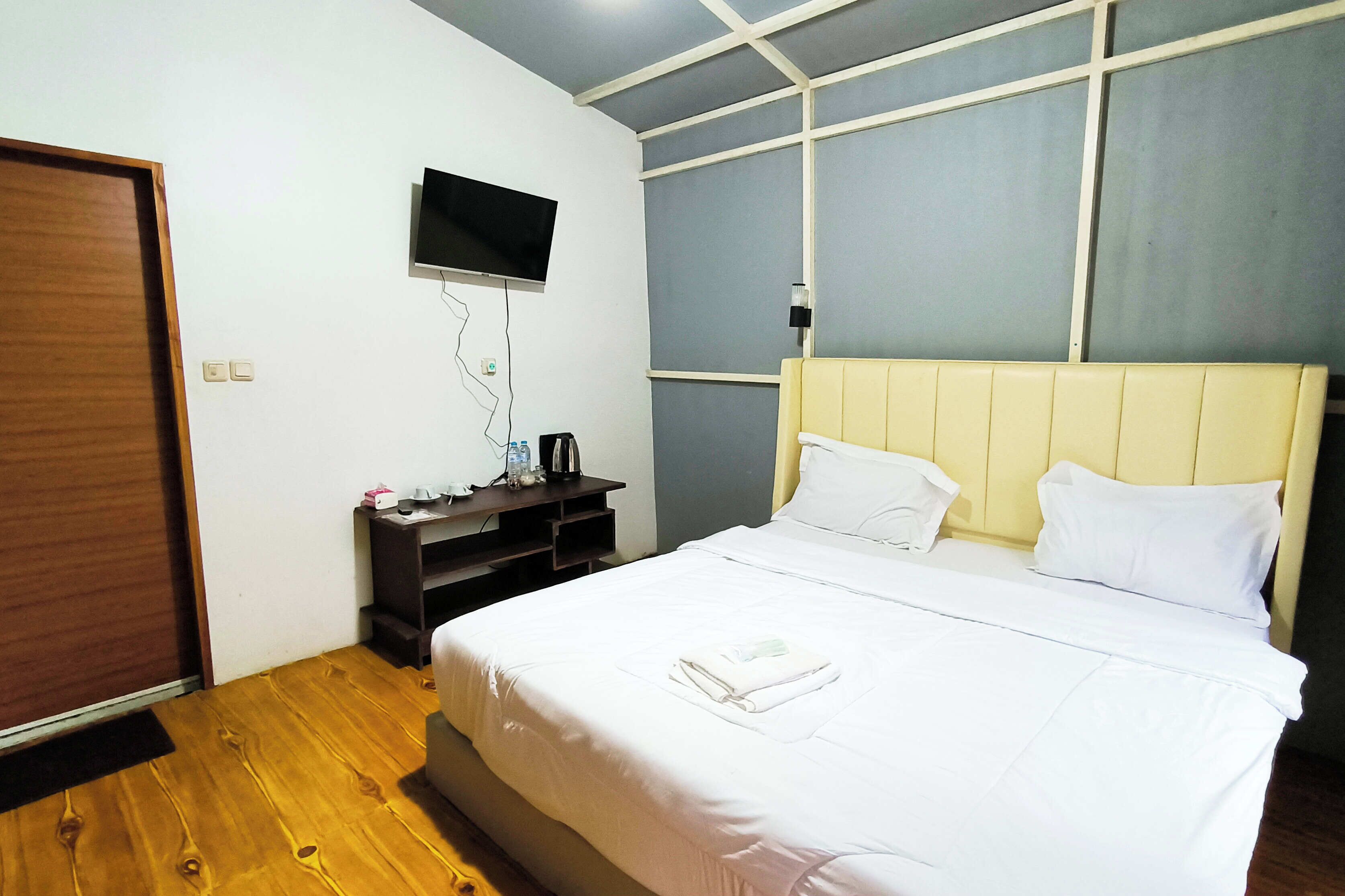 Habitación de hotel con cama, televisor montado en la pared, piso de madera y una puerta.