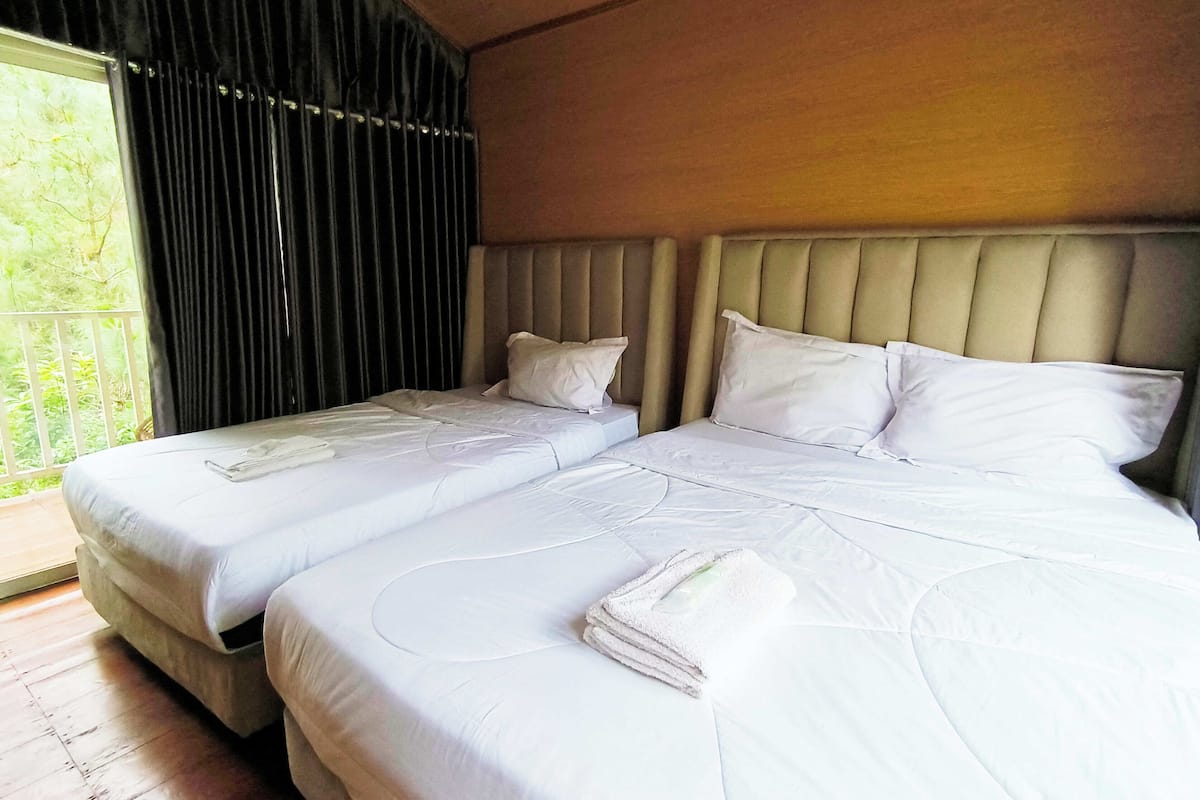 Ein Hotelzimmer mit zwei Betten, einem großen Fenster mit Vorhängen und Holzboden.