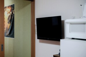 Ein Zimmer mit einem an der Wand befestigten Flachbildfernseher, einem weißen Schrank darunter und einer Tür mit einem Poster.