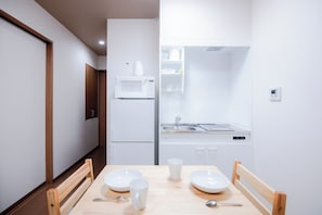 Eine kleine Küche mit weißen Geräten, einem Spülbecken und einem Essbereich mit Tisch und Stühlen.