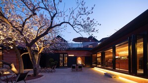 A modern building with a glass facade, outdoor seating area, and a tree with blossoms. - TOPSCAPE Yangshan Hotel (Qingdao)