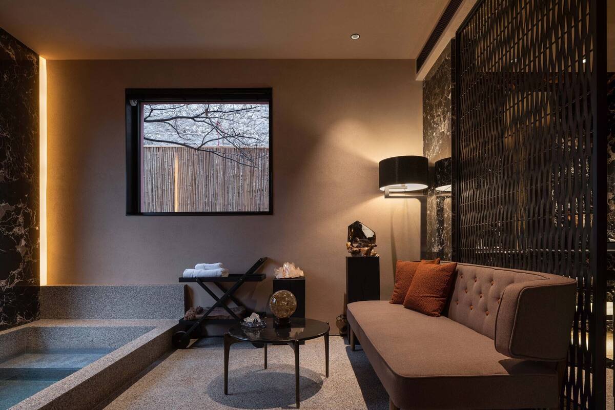 Una sala de estar moderna con un sofá, una mesa de centro y un ventanal con vistas a árboles desnudos.