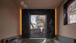 A modern bathroom with a stone wall, a built-in hot tub, and a large window offering a view of trees and a stone wall outside. - TOPSCAPE Yangshan Hotel (Qingdao)