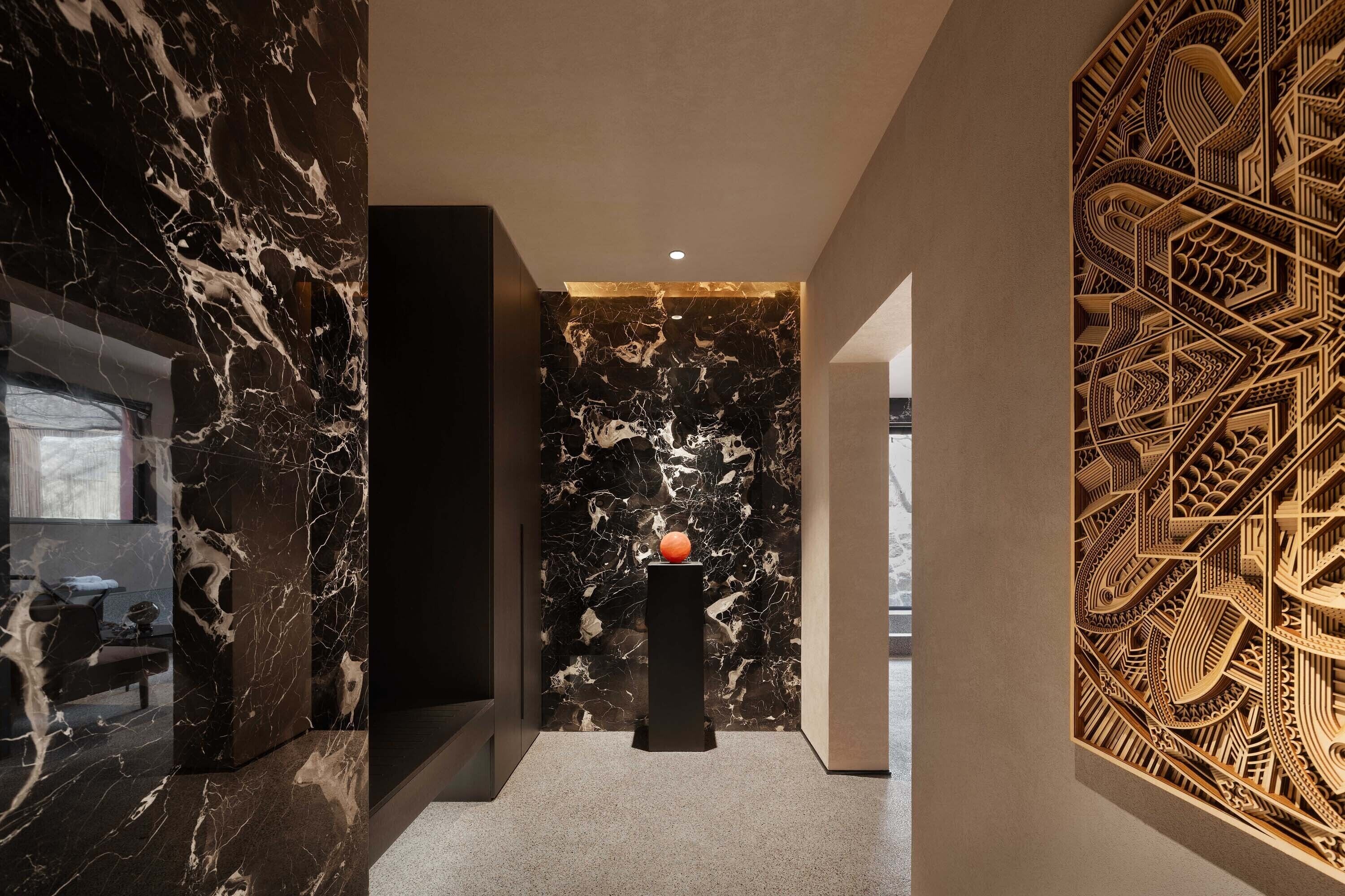 A modern hallway with marble walls, a black pedestal with a spherical object, and a detailed wooden panel.