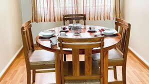 Uma área de refeições com uma mesa redonda de madeira posta para quatro pessoas, rodeada por cadeiras de madeira com assentos acolchoados.