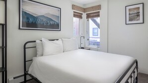 Ein ordentlich bezogenes Bett in einem Hotelzimmer, darüber ein Gemälde mit einer Berglandschaft.