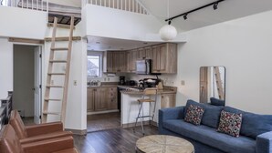 Eine moderne Loftlösung mit Schlafgalerie, einer Küche mit Holzausstattung, einem blauen Sofa und einem runden Couchtisch.