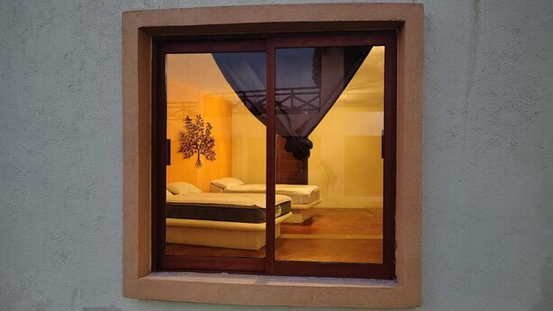 Een slaapkamer met een bed, nachtkastje en raam met uitzicht op een gebouw.