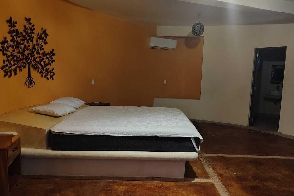 A bedroom with a bed, a nightstand, a wall decoration, and an air conditioning unit.
