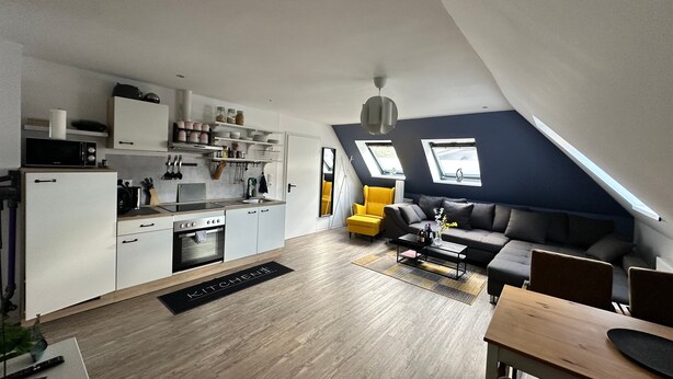 Un appartement moderne de style « loft », comprenant une cuisine, un coin repas et un espace de vie, avec des fenêtres de toit et un lit en mezzanine.