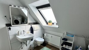 Une salle de bain moderne dotée d’une lucarne, d’un lavabo, de toilettes et d’une étagère où sont rangés les articles de toilette.