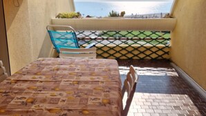 Un balcón con mesa y sillas, vista al mar y una cerca con celosía.