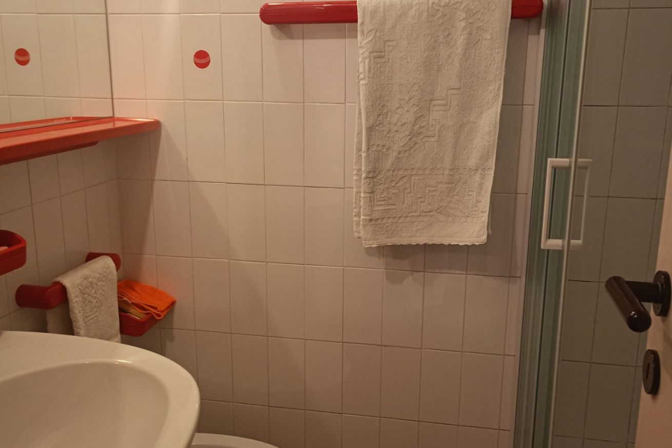 Une salle de bain avec un lavabo blanc, un porte-serviettes rouge et une porte de douche en verre.