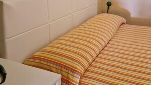 Una cama con ropa de cama a rayas, un cabecero blanco y una mesita de noche con un objeto verde encima.