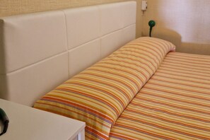 A bed with striped bedding, a white headboard, and a bedside table with a green object on it.