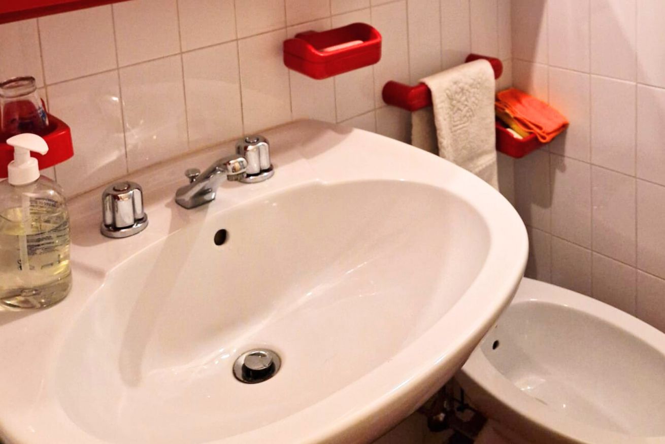 Une salle de bain avec un lavabo blanc, deux robinets, un distributeur de savon en verre et un bidet.