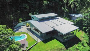 Ett modernt hus i två våningar med en swimmingpool, omgivet av frodig grönska.