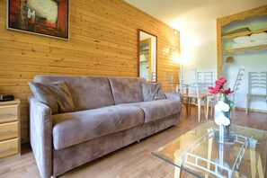A wooden-paneled room with a sofa, a glass coffee table, and a painting on the wall. - Apartment in 3 Vallees With Pool & Sauna (Orelle)