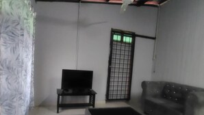 A room with a grey sofa, a black ottoman, a small black table with a television, and a ceiling fan.