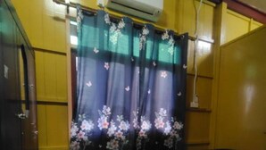 A room with yellow walls, a patterned green and white floor, a bed with a floral bedspread, and an air conditioning unit on the wall.