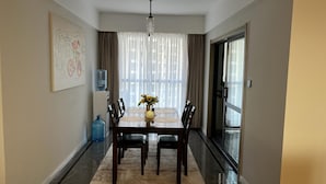 A dining area with a rectangular table, six chairs, a vase with flowers, a water dispenser, and a large window with curtains. - Parkview Cribs. Serene 3BR with a DSQ near JKIA and SGR with National park view. (Nairobi)