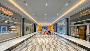 A modern shopping mall corridor with a checkered floor pattern, illuminated ceiling, and various retail stores on either side. - Vogue Park Tower DIFC  (Dubai)