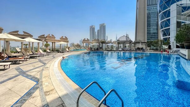 A swimming pool with lounge chairs and umbrellas, surrounded by modern buildings. - Vogue Park Tower DIFC  (Dubai)